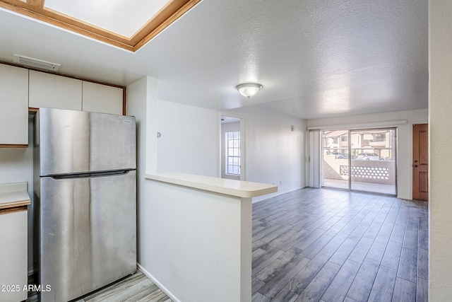 kitchen featuring white cabinets, stainless steel fridge, light wood-type flooring, and kitchen peninsula