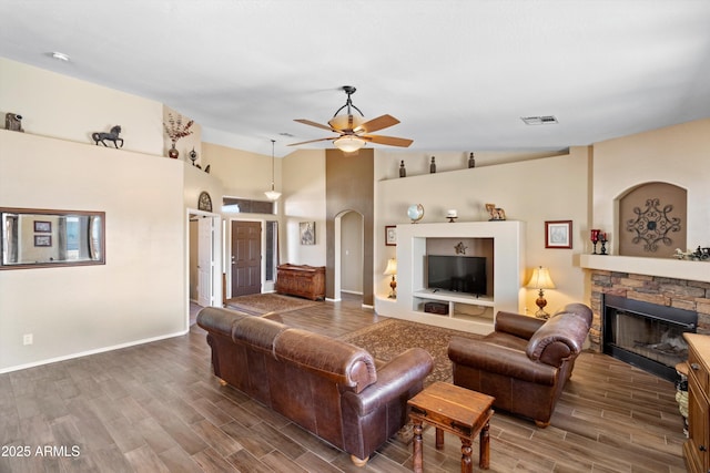 living room featuring a stone fireplace, wood finish floors, visible vents, and ceiling fan