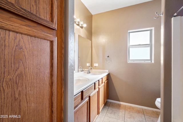 bathroom with baseboards, double vanity, a sink, tile patterned floors, and toilet