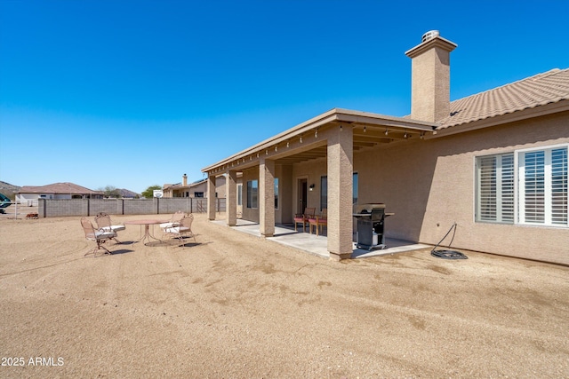 back of house with stucco siding, a chimney, a patio, and fence