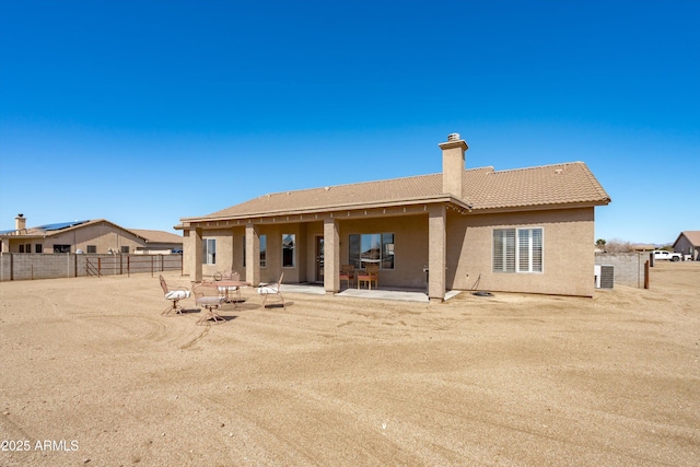 rear view of house with stucco siding, a patio, fence, a chimney, and a tiled roof