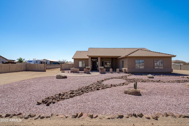 rear view of property with stucco siding, a tiled roof, and fence