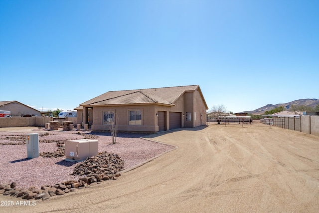 rear view of property with an attached garage, fence, a tile roof, stucco siding, and driveway