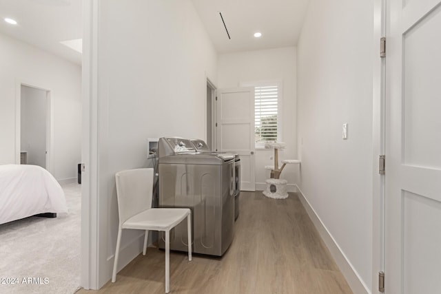 clothes washing area with washing machine and dryer and light wood-type flooring