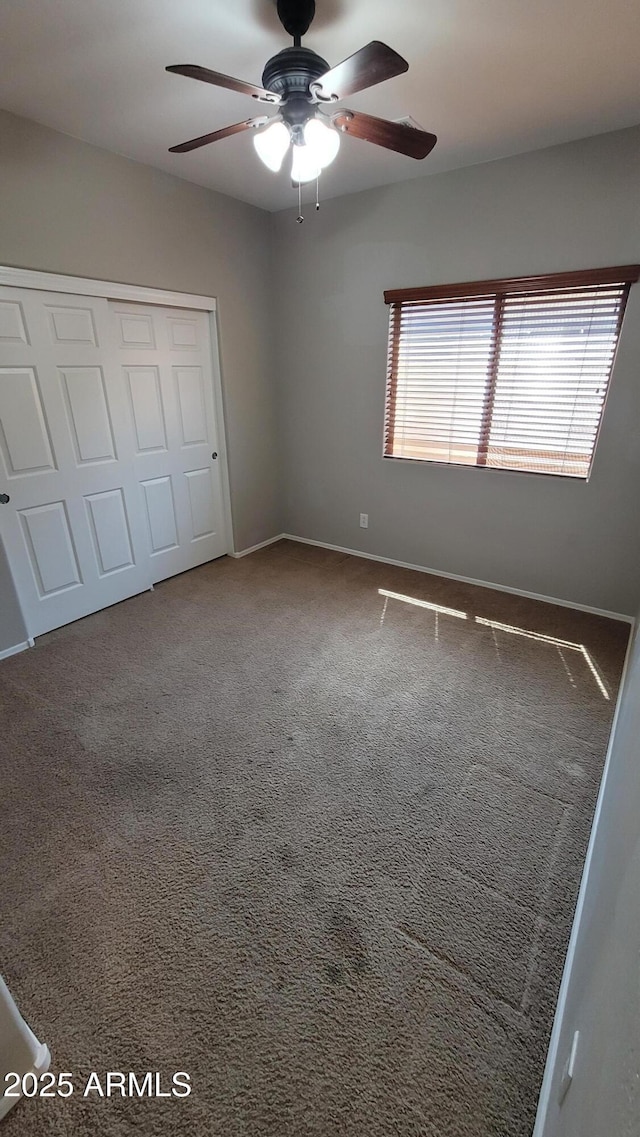unfurnished bedroom with a closet, baseboards, carpet floors, and a ceiling fan