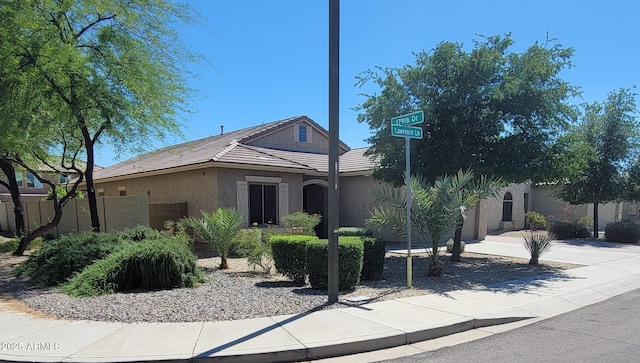 ranch-style home with stucco siding, a tiled roof, driveway, and fence