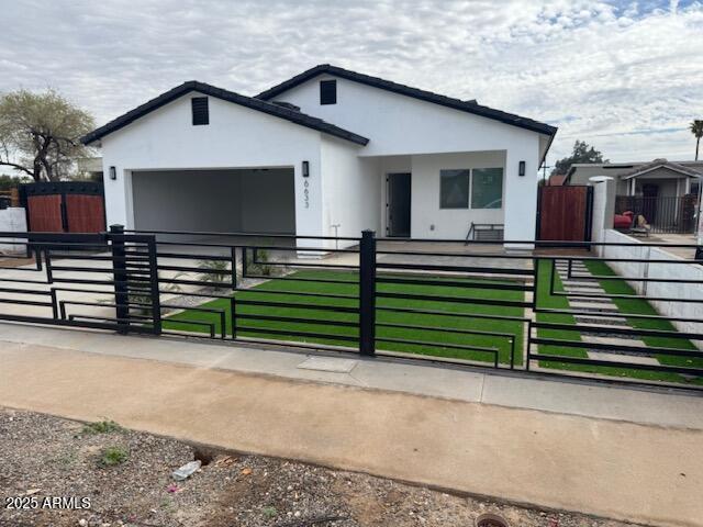 view of front facade with stucco siding, a garage, a fenced front yard, and a gate