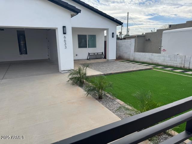 rear view of house with stucco siding, a lawn, and fence