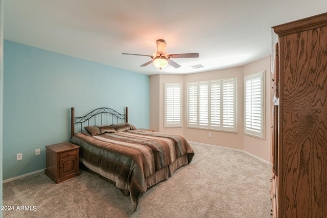 bedroom with light colored carpet, ceiling fan, visible vents, and baseboards