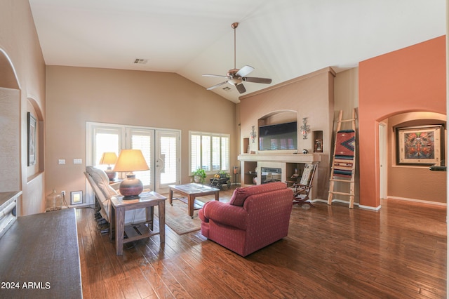 living room featuring dark wood-style floors, visible vents, a ceiling fan, a glass covered fireplace, and high vaulted ceiling