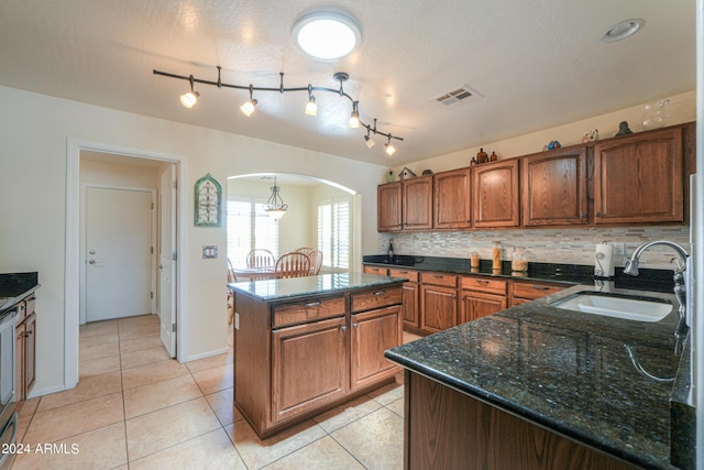 kitchen featuring visible vents, arched walkways, a center island, a sink, and backsplash