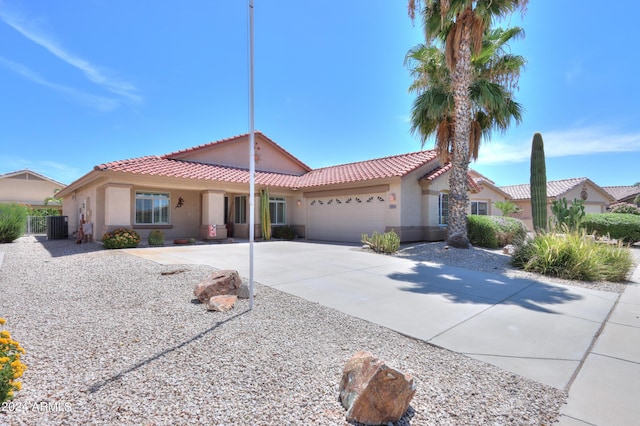 view of front of house featuring a garage, driveway, a tile roof, central AC, and stucco siding