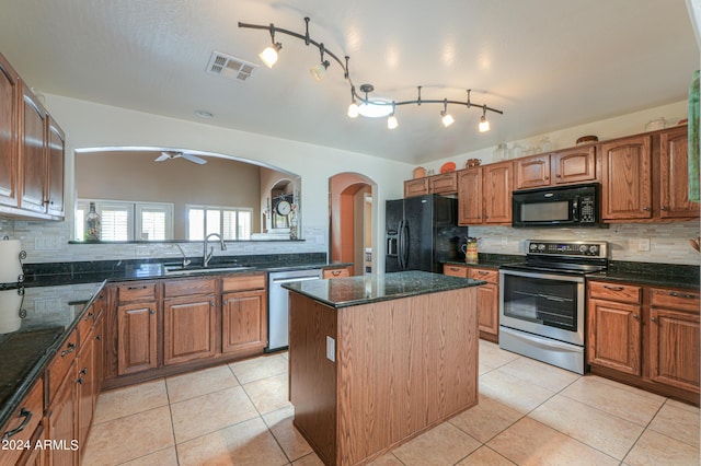 kitchen with a sink, visible vents, a center island, dark stone counters, and black appliances