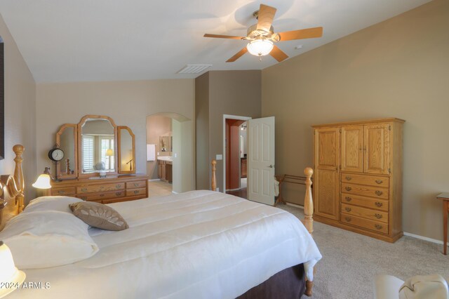 bedroom featuring arched walkways, lofted ceiling, ensuite bathroom, light carpet, and visible vents