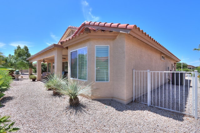 view of side of home with a tile roof, stucco siding, a patio area, ceiling fan, and fence