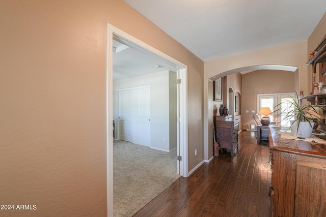 hall featuring arched walkways, dark wood finished floors, and baseboards