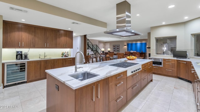 kitchen with sink, white cooktop, island range hood, beverage cooler, and a kitchen island with sink