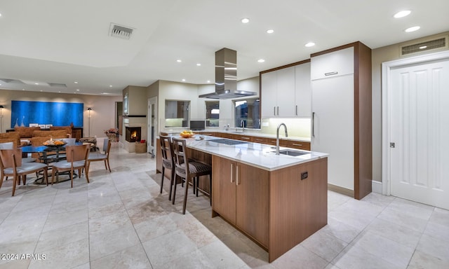 kitchen with a kitchen bar, a center island with sink, island exhaust hood, and sink