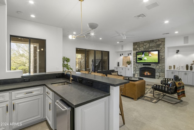 kitchen featuring white cabinets, a kitchen breakfast bar, a stone fireplace, sink, and kitchen peninsula