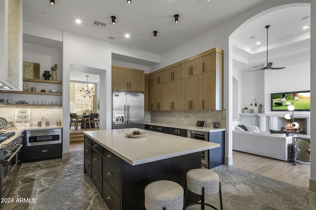 kitchen with decorative backsplash, ceiling fan, built in appliances, hardwood / wood-style floors, and a center island