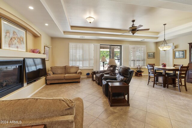 tiled living room with a raised ceiling and ceiling fan with notable chandelier