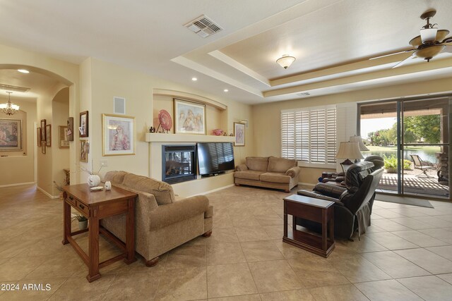 living room with ceiling fan with notable chandelier, a tray ceiling, and light tile patterned floors