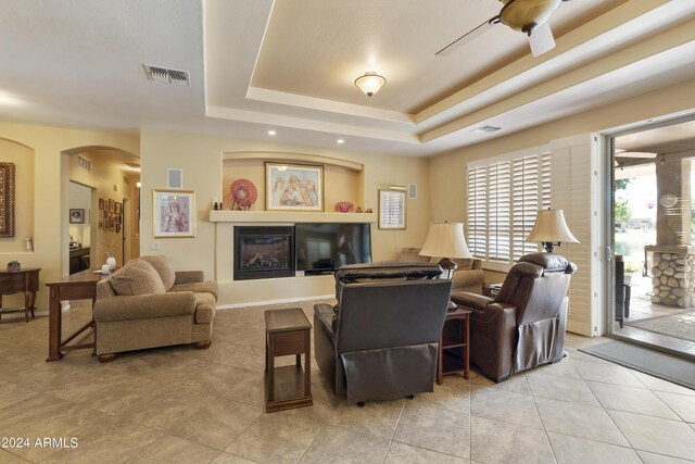 living room with light tile patterned floors, a tray ceiling, and ceiling fan