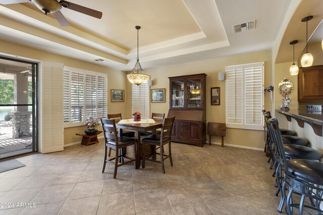 tiled dining room with ceiling fan, a raised ceiling, and a healthy amount of sunlight