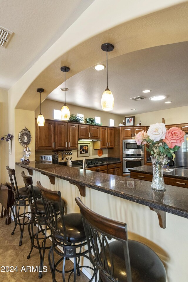 kitchen with stainless steel appliances, hanging light fixtures, kitchen peninsula, and a breakfast bar