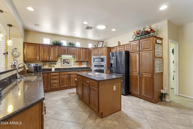 kitchen featuring appliances with stainless steel finishes, a kitchen island, decorative light fixtures, dark stone counters, and sink