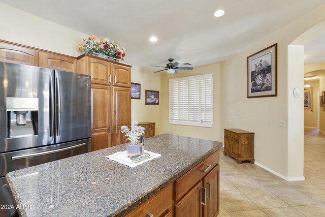 kitchen featuring ceiling fan, stainless steel refrigerator with ice dispenser, dark stone counters, and light tile patterned floors