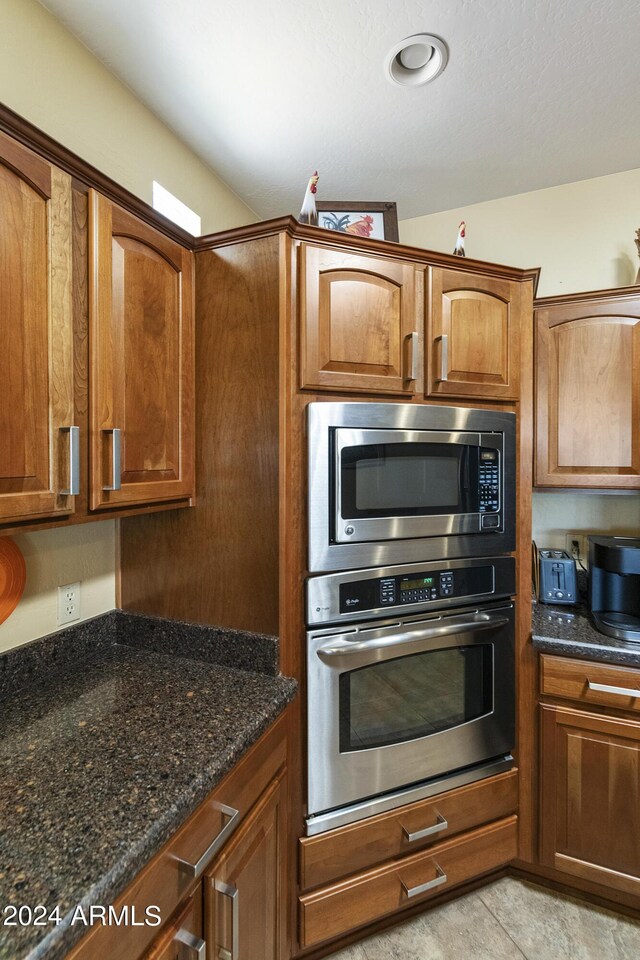 kitchen with appliances with stainless steel finishes, light tile patterned floors, and dark stone counters