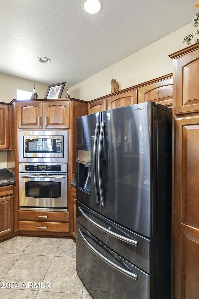 kitchen with dark stone counters, stainless steel appliances, a textured ceiling, and light tile patterned flooring