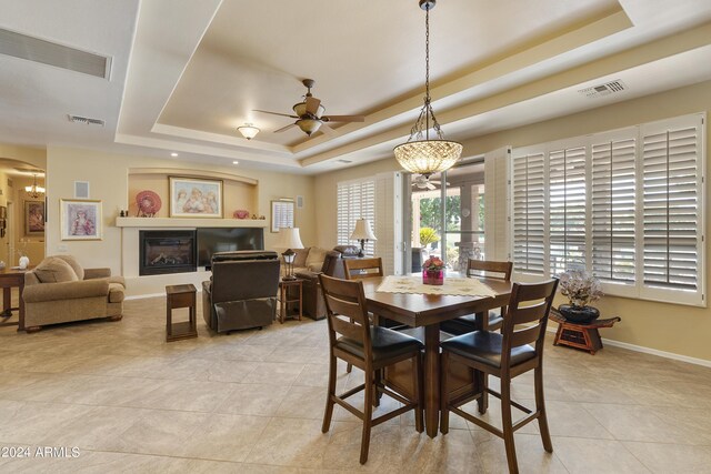 dining area with ceiling fan with notable chandelier, a raised ceiling, and light tile patterned floors