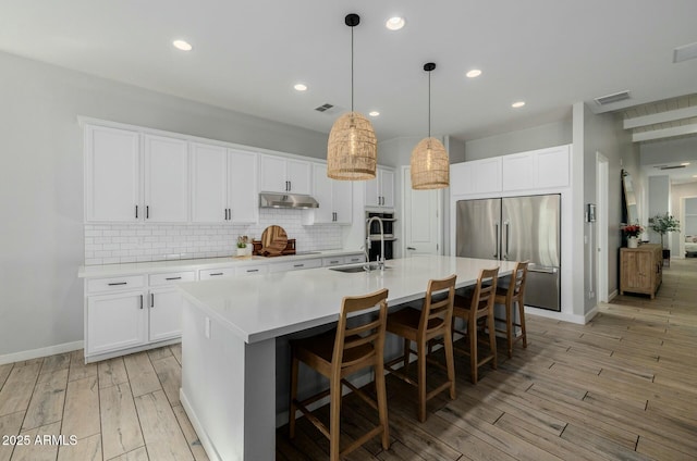 kitchen featuring tasteful backsplash, light wood-style flooring, appliances with stainless steel finishes, under cabinet range hood, and a sink