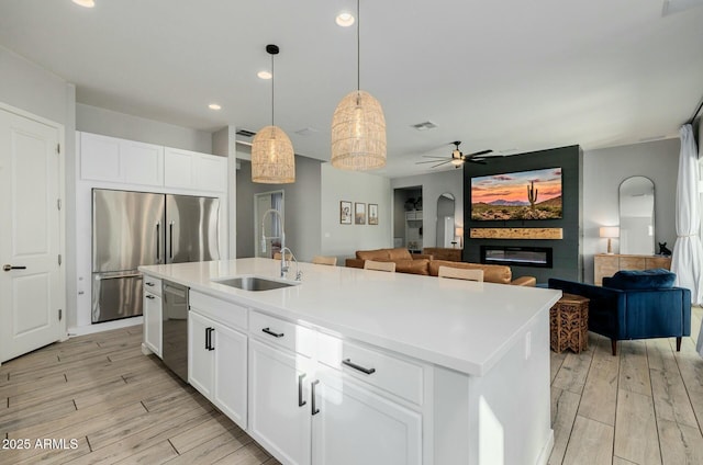 kitchen featuring a large fireplace, stainless steel appliances, a sink, and light wood finished floors