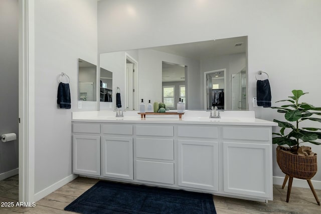 bathroom with double vanity, baseboards, wood finished floors, an enclosed shower, and a sink