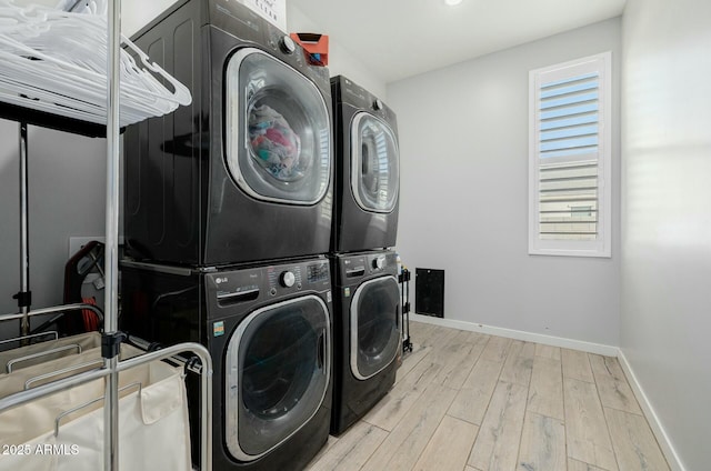 washroom featuring stacked washer and dryer, wood finished floors, laundry area, and baseboards