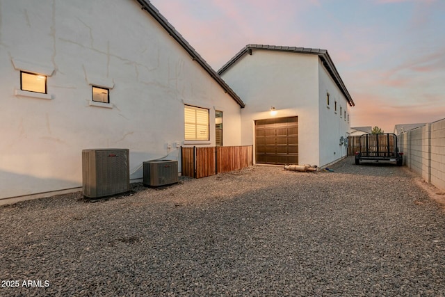 back of house with central air condition unit, an attached garage, fence, and stucco siding