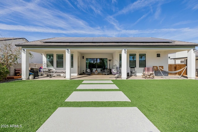 back of property with a yard, a patio area, fence, and roof mounted solar panels