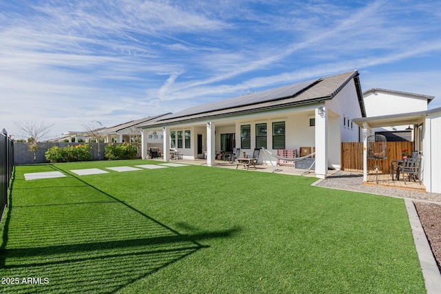 rear view of house featuring a lawn, a patio area, a fenced backyard, and roof mounted solar panels