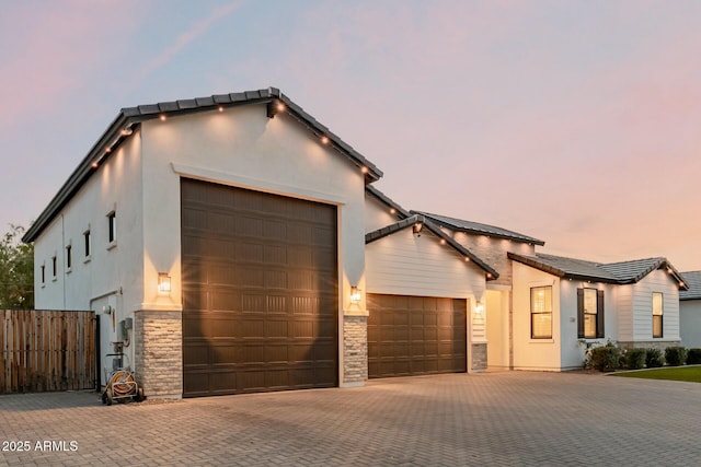 view of front of property with decorative driveway, stone siding, fence, and stucco siding