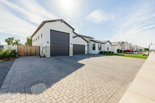 view of front of home featuring decorative driveway, stucco siding, an attached garage, a gate, and fence