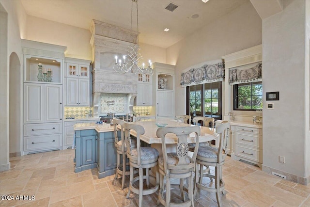 kitchen with backsplash, white cabinets, hanging light fixtures, and a center island with sink