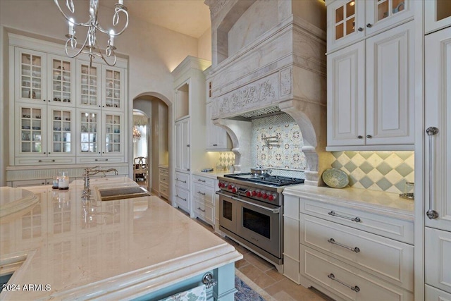 kitchen with sink, tasteful backsplash, premium range hood, double oven range, and decorative light fixtures