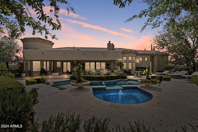 pool at dusk featuring an in ground hot tub and a patio