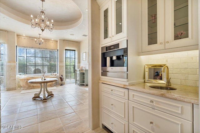 bathroom featuring a washtub, vanity, a raised ceiling, and a notable chandelier