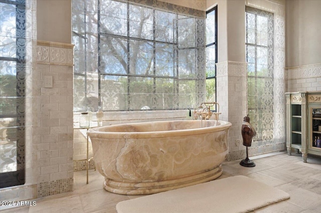 bathroom with tile patterned flooring, a bath, and tile walls