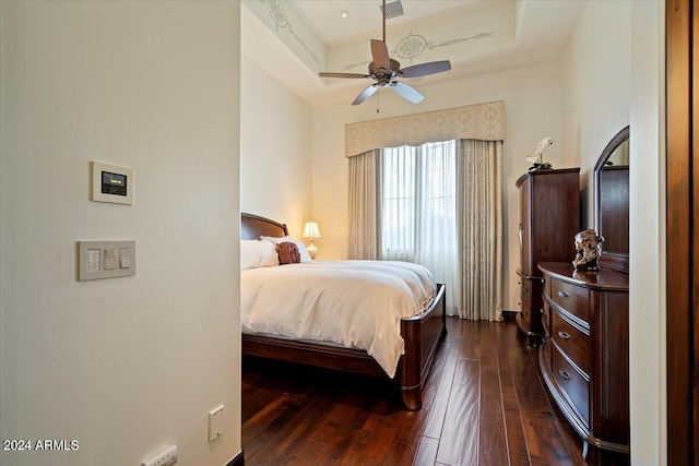 bedroom with a raised ceiling, ceiling fan, and dark wood-type flooring