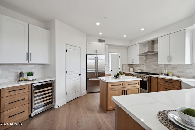 kitchen featuring white cabinets, wine cooler, wall chimney exhaust hood, decorative backsplash, and premium appliances